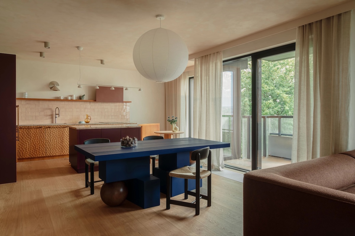 Interior of Studio Bosko with a dark blue dining table, warm wood tones, glazed kitchen tiles and soft curtains in an open living space.
