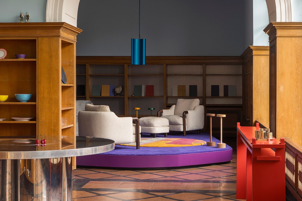 Interior by Gisbert Pöppler with timber cladding, colourful accents, a blue pendant light and a circular purple platform with armchairs in a historic space.