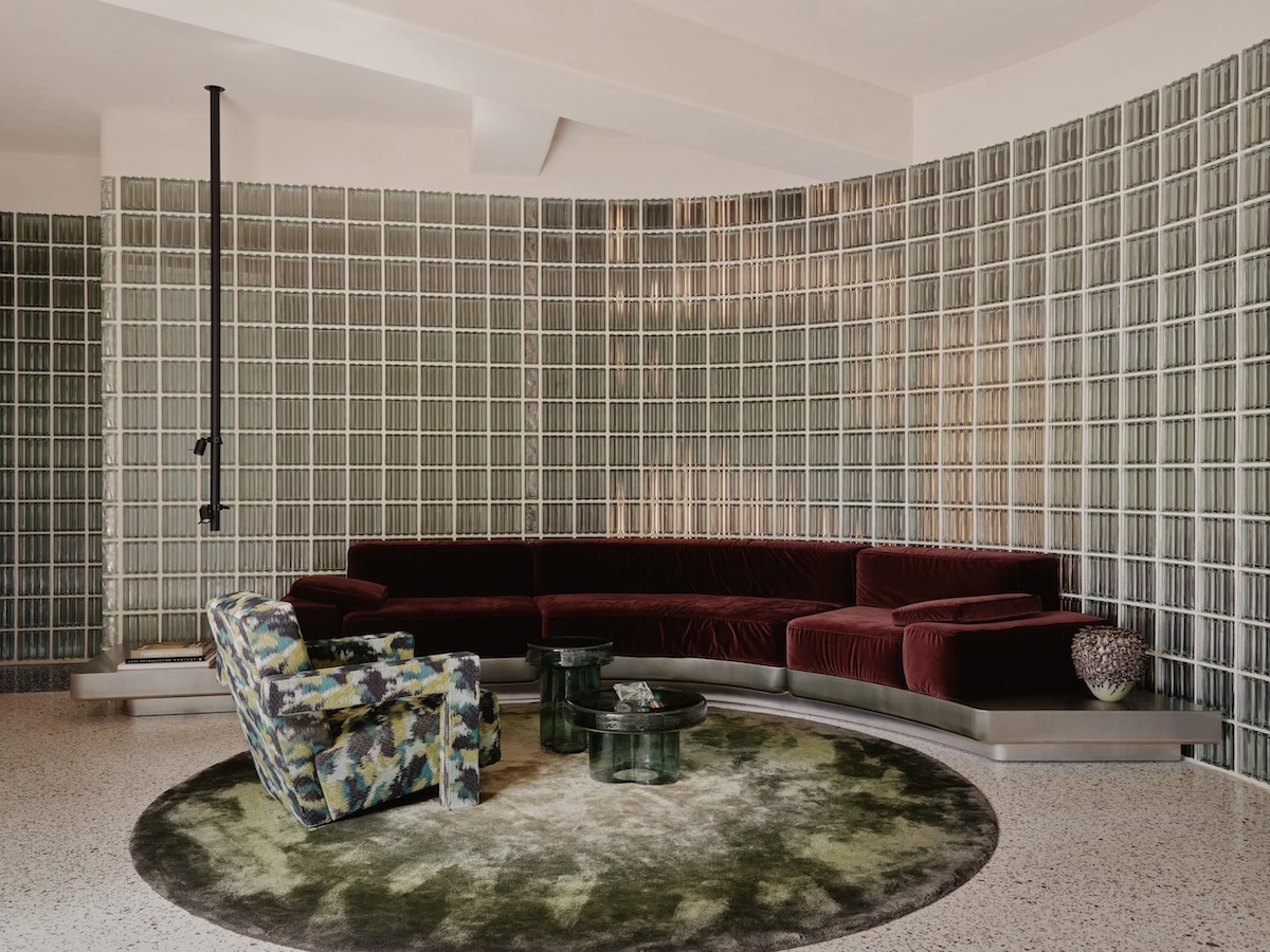 Interior by Studio Karhard for Berghain with a full glass-block wall, a wine-red modular sofa, a bold patterned armchair and a dark-toned rug.