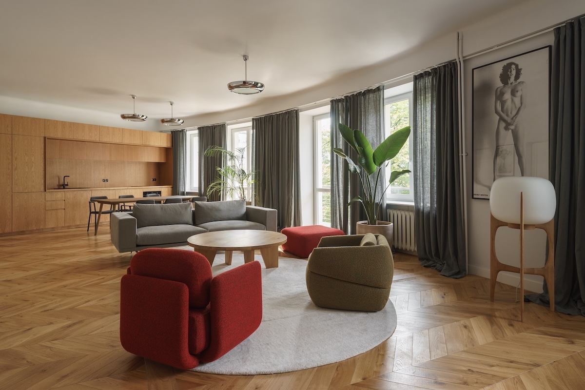 Interior of Studio Loft Kolasiński with parquet flooring, built-in oak furniture, a grey sofa, a red armchair and a muted palette linking vintage and contemporary design.